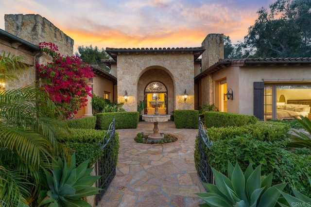 exterior entry at dusk with a patio area, a chimney, stone siding, and stucco siding