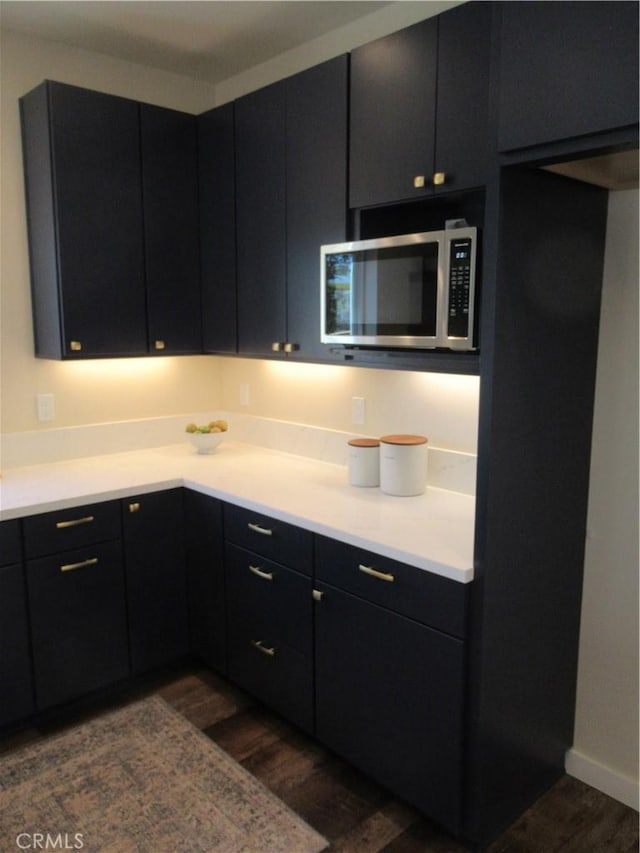 kitchen featuring light countertops, dark wood-type flooring, stainless steel microwave, and dark cabinets