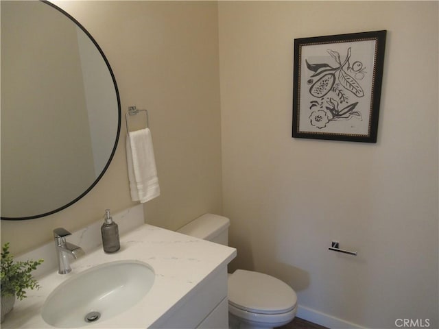 half bathroom featuring toilet, baseboards, and vanity