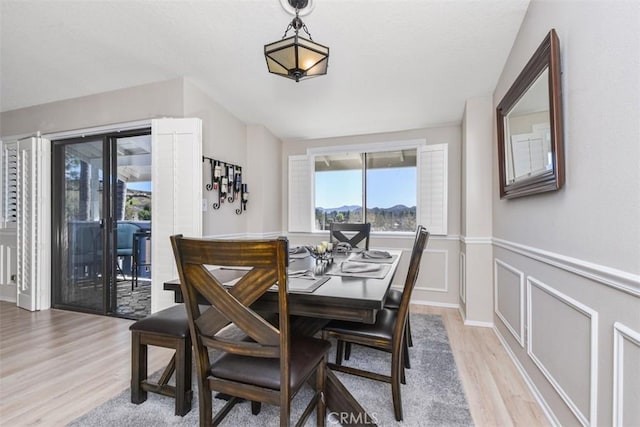 dining space featuring light wood-style floors, a wainscoted wall, and a decorative wall