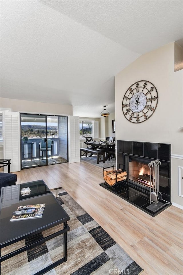 living room with a tile fireplace, vaulted ceiling, a textured ceiling, and wood finished floors