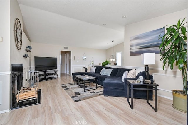 living area with vaulted ceiling, light wood-style flooring, and visible vents