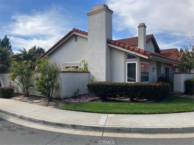 view of side of property with a chimney, a lawn, a tiled roof, and stucco siding