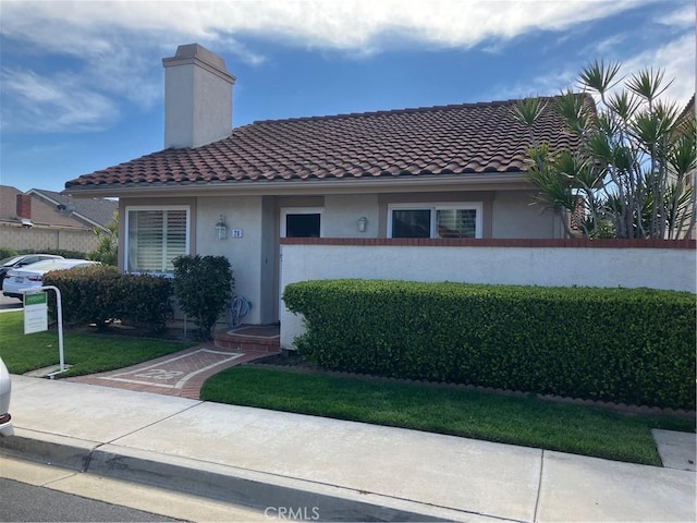 view of front of property with a tile roof, a front yard, a chimney, and stucco siding