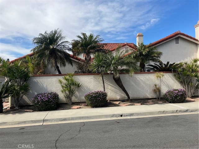 view of side of property with a tiled roof, fence, and stucco siding