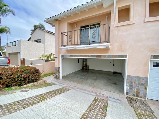 exterior space with stucco siding, a garage, a balcony, and fence