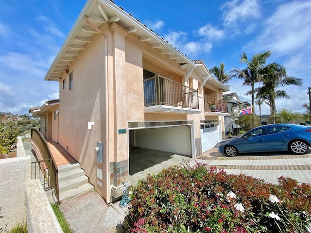 view of property exterior with a garage, stucco siding, driveway, and a balcony