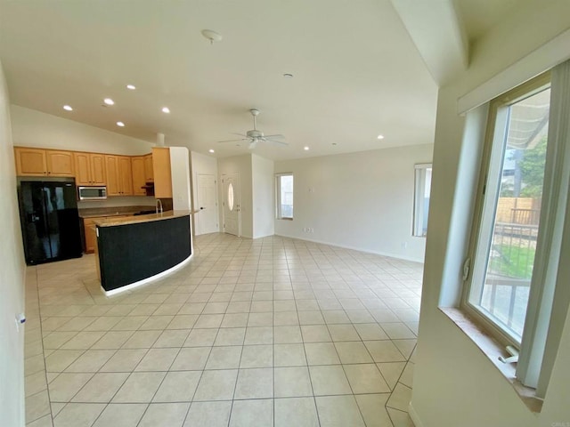 kitchen featuring vaulted ceiling, a sink, open floor plan, stainless steel microwave, and freestanding refrigerator