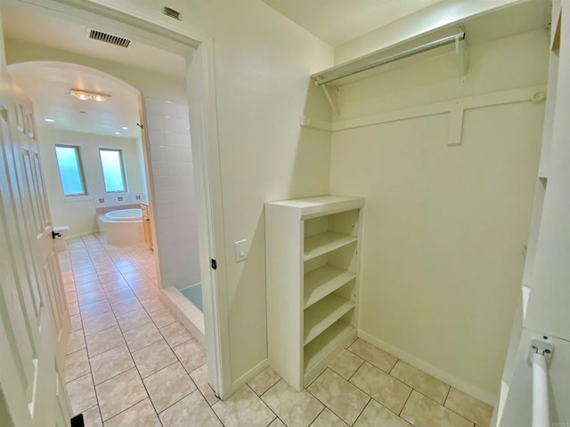 spacious closet featuring visible vents, arched walkways, and light tile patterned floors
