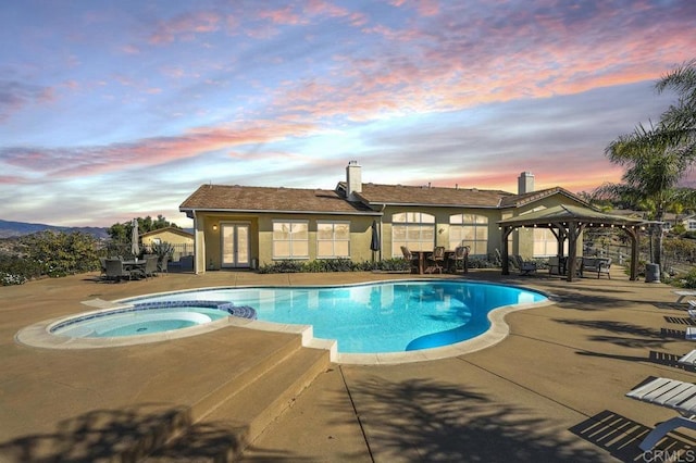 pool at dusk with a gazebo, a patio area, and a pool with connected hot tub