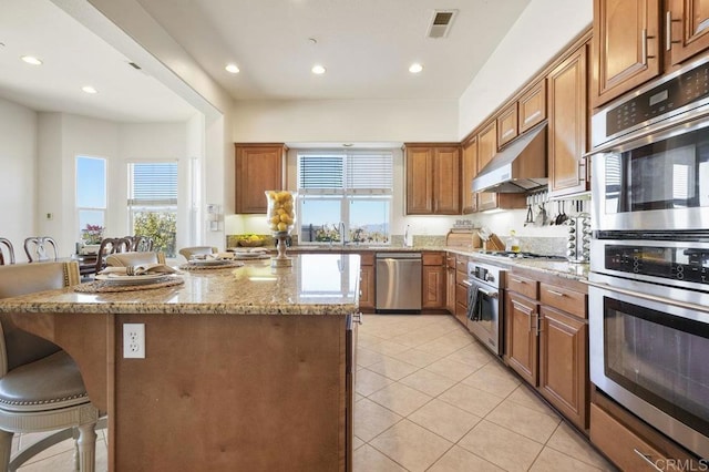 kitchen featuring a kitchen island, light stone counters, a kitchen breakfast bar, stainless steel appliances, and under cabinet range hood