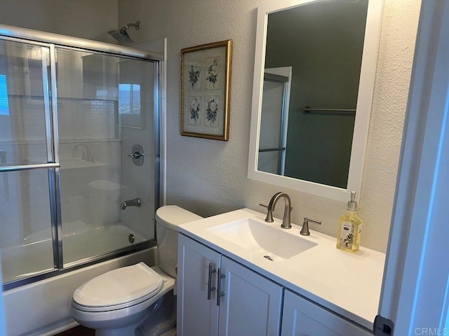 full bath with a textured wall, bath / shower combo with glass door, vanity, and toilet