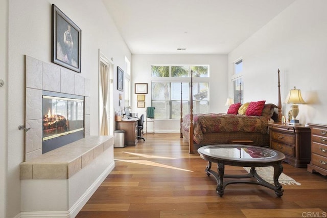 bedroom with visible vents, a tiled fireplace, baseboards, and wood finished floors