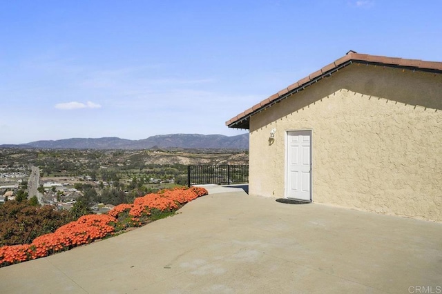 view of side of property with a patio area, a mountain view, fence, and stucco siding