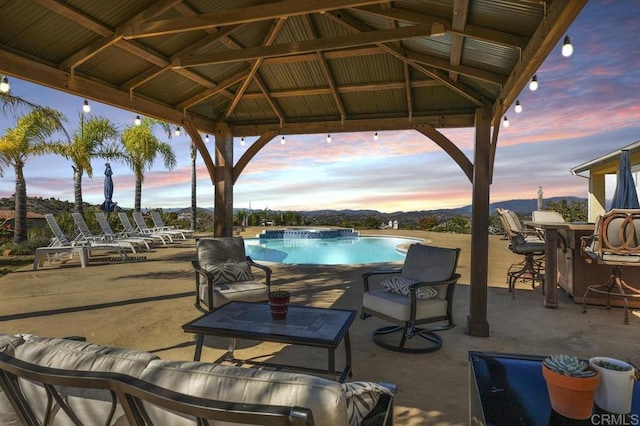 pool at dusk featuring an outdoor bar, an outdoor pool, and a gazebo