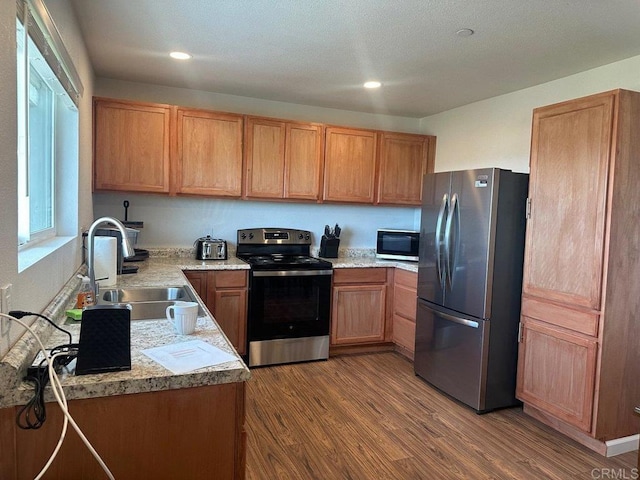 kitchen featuring brown cabinets, wood finished floors, stainless steel appliances, light countertops, and a sink