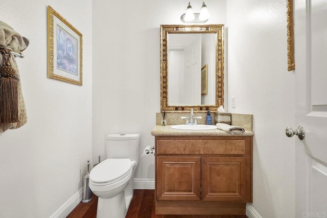 bathroom featuring toilet, baseboards, wood finished floors, and vanity