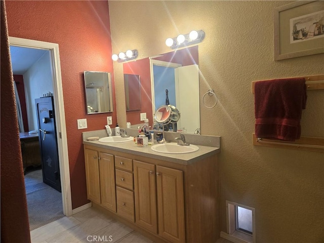 full bathroom with double vanity, a textured wall, a sink, and tile patterned floors