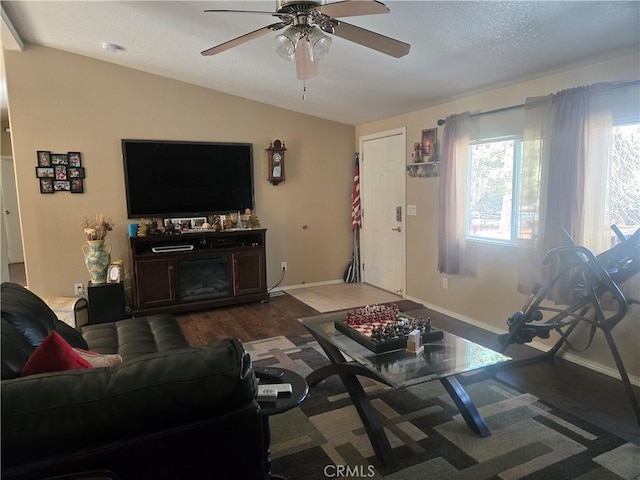 living room featuring baseboards, a ceiling fan, vaulted ceiling, and dark wood-type flooring