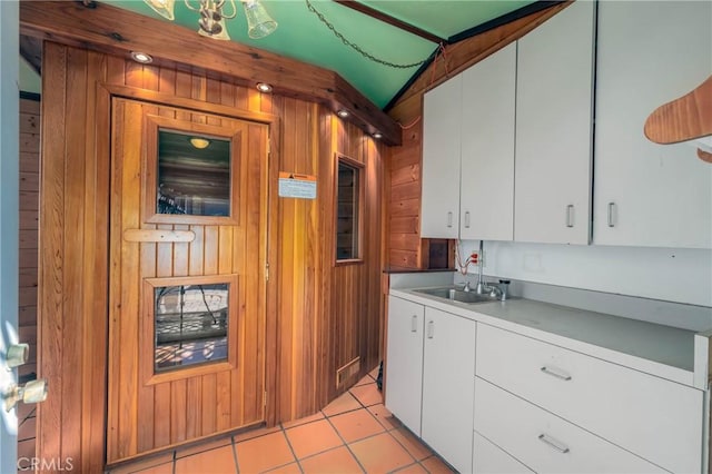 kitchen with light tile patterned floors, wooden walls, white cabinets, light countertops, and a sink