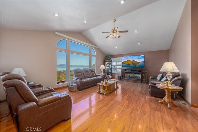 living area with a glass covered fireplace, ceiling fan, baseboards, and wood finished floors