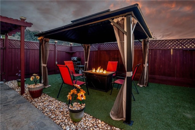 patio terrace at dusk with a yard, a gazebo, an outdoor fire pit, and a fenced backyard