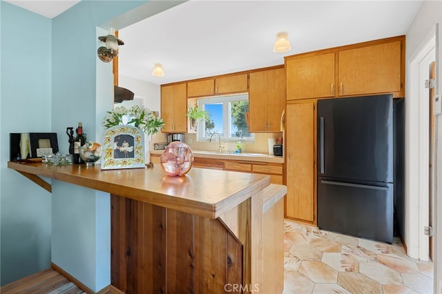 kitchen featuring a peninsula, a sink, light countertops, freestanding refrigerator, and brown cabinets