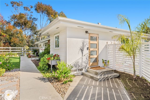 view of exterior entry featuring fence and stucco siding