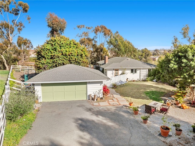 ranch-style home with roof with shingles, a detached garage, fence, and an outdoor structure