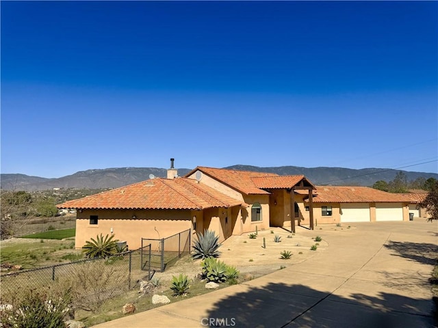 view of front of home featuring a mountain view, fence, driveway, a tiled roof, and stucco siding