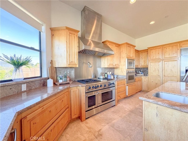 kitchen with recessed lighting, appliances with stainless steel finishes, wall chimney range hood, light brown cabinetry, and tasteful backsplash