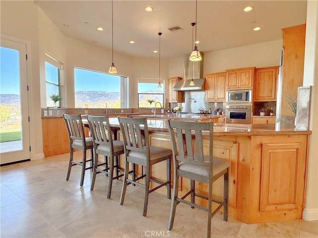 kitchen featuring a mountain view, light countertops, appliances with stainless steel finishes, wall chimney range hood, and decorative light fixtures