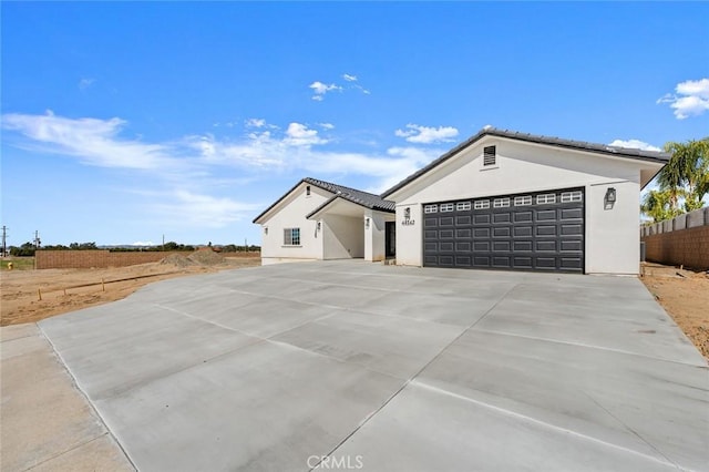 view of front facade with a garage, concrete driveway, a tile roof, fence, and stucco siding