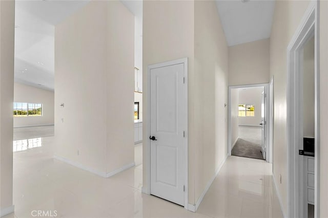 hallway with light tile patterned flooring, a towering ceiling, and baseboards