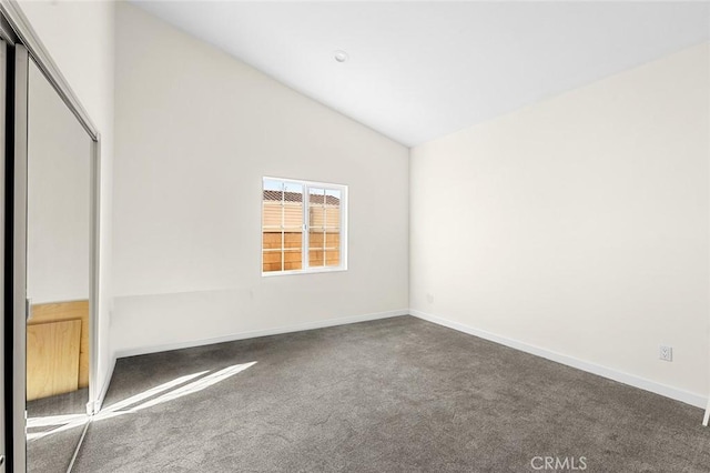 unfurnished bedroom featuring dark carpet, a closet, vaulted ceiling, and baseboards