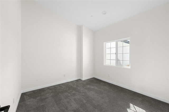 spare room featuring baseboards and dark carpet