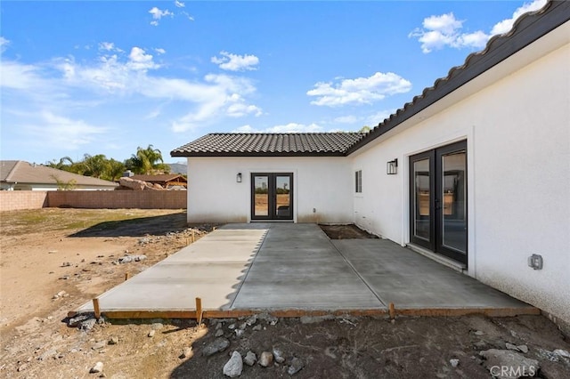 rear view of house featuring french doors, stucco siding, a patio area, fence, and a tiled roof