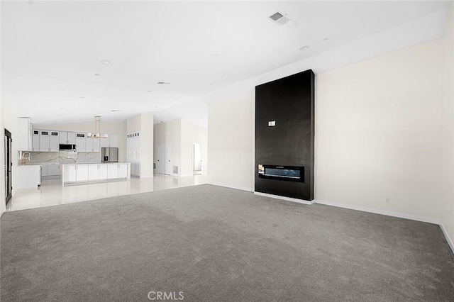 unfurnished living room featuring lofted ceiling, light colored carpet, visible vents, a sink, and baseboards