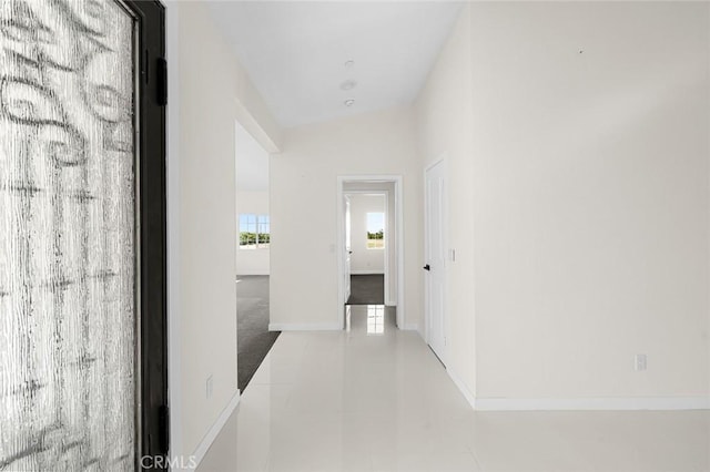 hall with vaulted ceiling, tile patterned flooring, and baseboards