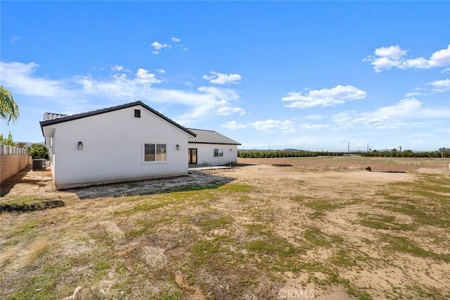 rear view of house with a rural view, fence, and stucco siding