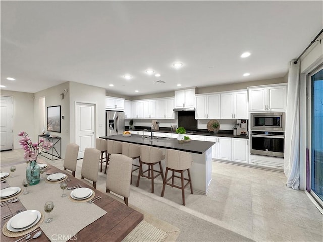 kitchen featuring a breakfast bar, a sink, white cabinets, appliances with stainless steel finishes, and dark countertops