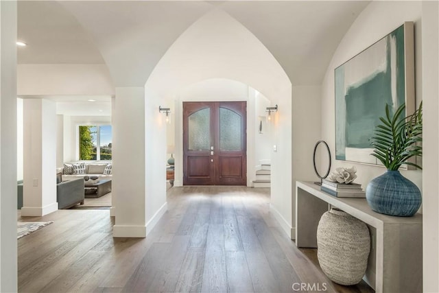 foyer with arched walkways, lofted ceiling, baseboards, and wood finished floors