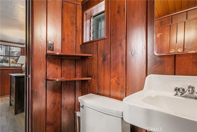 half bathroom with a sink, wooden walls, and toilet