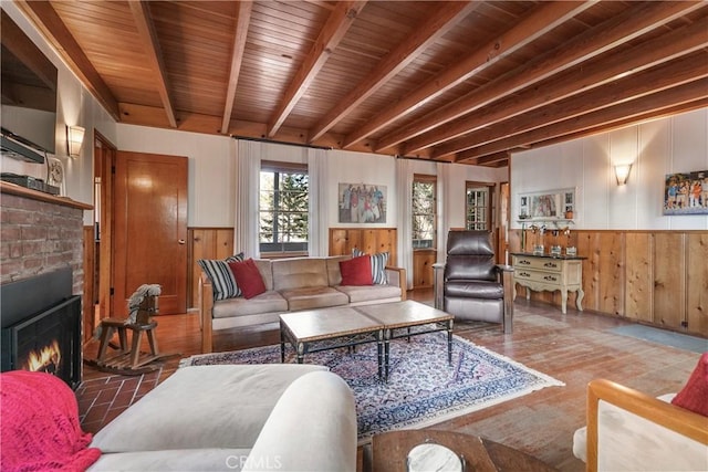 living room featuring beam ceiling, a wainscoted wall, a brick fireplace, wood walls, and wooden ceiling