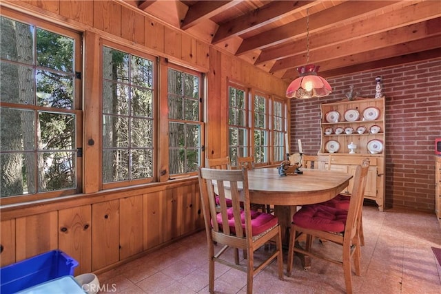 dining space with brick wall, a wealth of natural light, wood walls, and beam ceiling