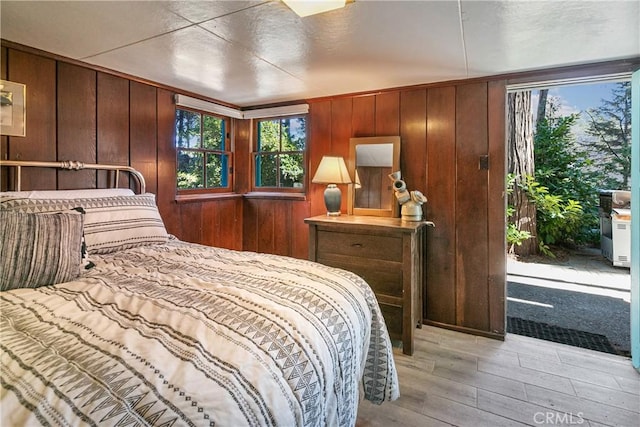 bedroom with light wood-style floors, multiple windows, and wood walls