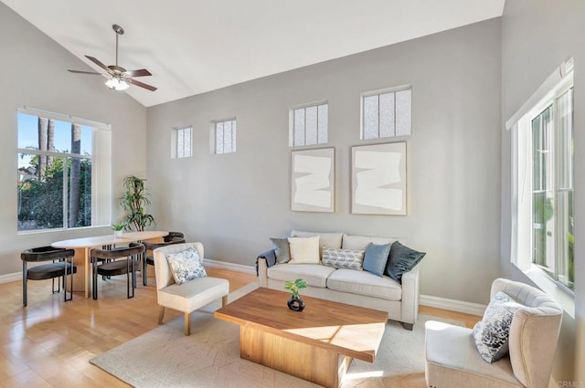 living area with baseboards, ceiling fan, high vaulted ceiling, and light wood-style floors