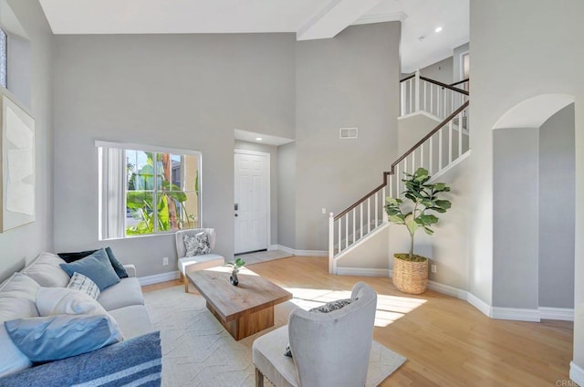 living room with baseboards, arched walkways, a towering ceiling, stairs, and light wood-style floors