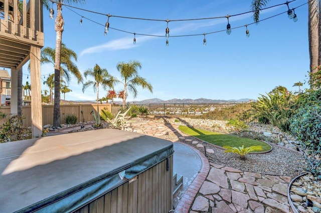 view of patio featuring a balcony, a hot tub, a mountain view, and a fenced backyard