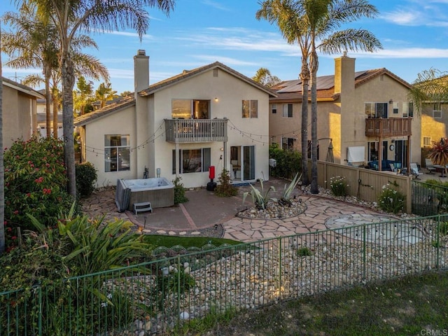 rear view of house featuring a hot tub, a patio, a balcony, a fenced backyard, and a chimney